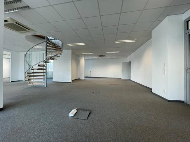 Heller Büroraum mit einer modernen Wendeltreppe und weiß gestrichenen Wänden, bereit zur individuellen Gestaltung.