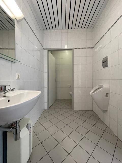 Sanitärbereich mit weißen Fliesen, Waschbecken und einem Urinal, sauber und funktional gestaltet.