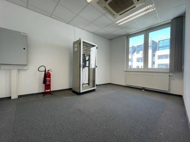 Büroraum mit Fenster, Heizkörper und einem Serverschrank, ausgestattet für technische Infrastruktur.
