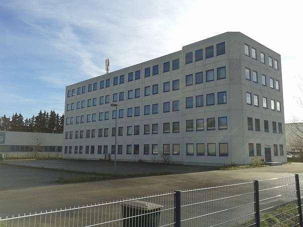 Großes, modernes Geschäftsgebäude mit grauer Fassade, vielen Fenstern und einem weitläufigen Parkplatzbereich.