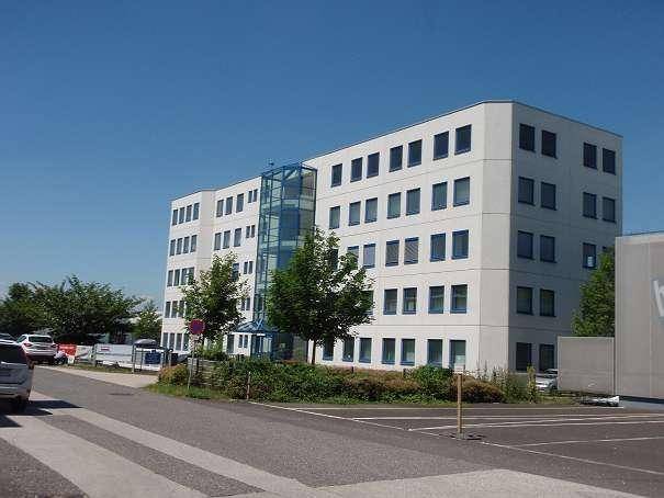 Modernes Bürogebäude mit weißer Fassade, zahlreichen Fenstern und einem gläsernen Aufzugsschacht an der Seite.