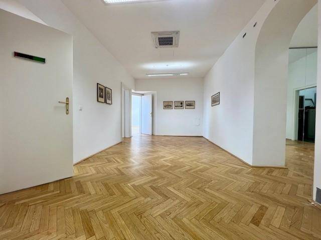 Langer Flur mit Fischgrätparkett und modernen Deckenleuchten, der zu verschiedenen Büroräumen führt.