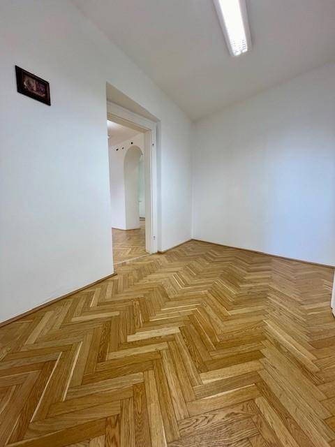 Heller Büroraum mit Fischgrätparkett und offenem Zugang zu einem Flur mit weiteren Räumen.