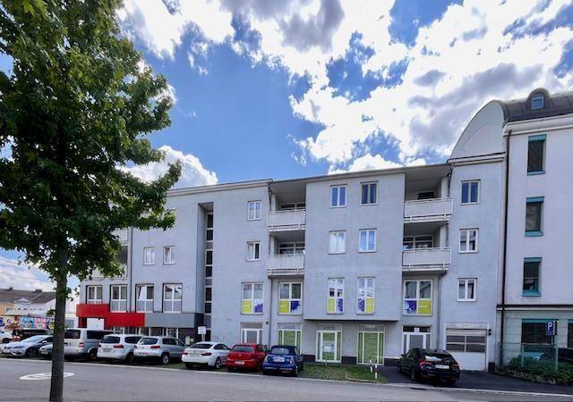 Ansicht eines modernen Wohngebäudes mit Balkonen und Parkplätzen vor der hellgrauen Fassade.