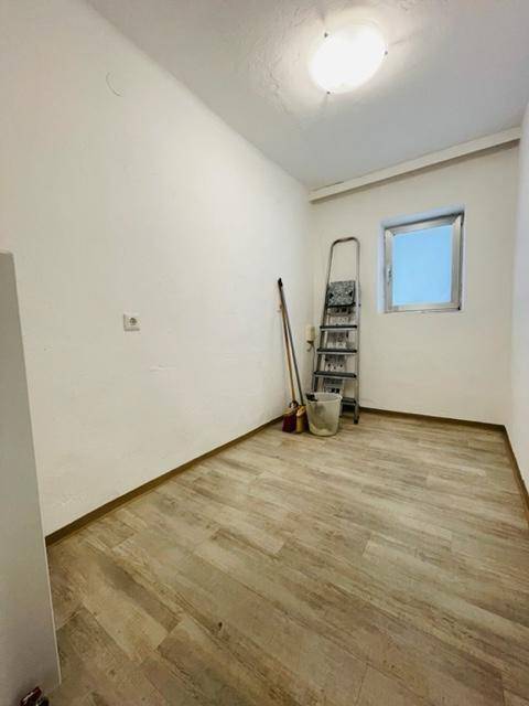 Kleiner, heller Raum mit Laminatboden und einem Fenster, ausgestattet mit einer Leiter.
