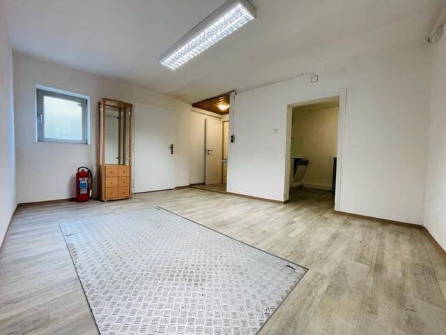 Raum mit Laminatboden, Fenster und einer Metallplatte am Boden, führt zu weiteren Räumen.
