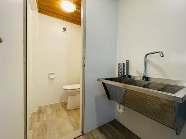 Kleiner Toilettenraum mit WC und separatem Waschbecken aus Edelstahl, Holzakzente an der Decke.