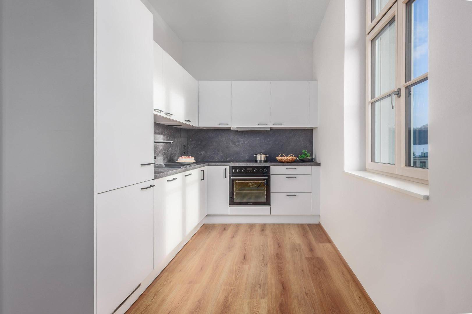 Helle, moderne Küche mit weißen Schränken, Holzboden und einem Fenster für Tageslicht.