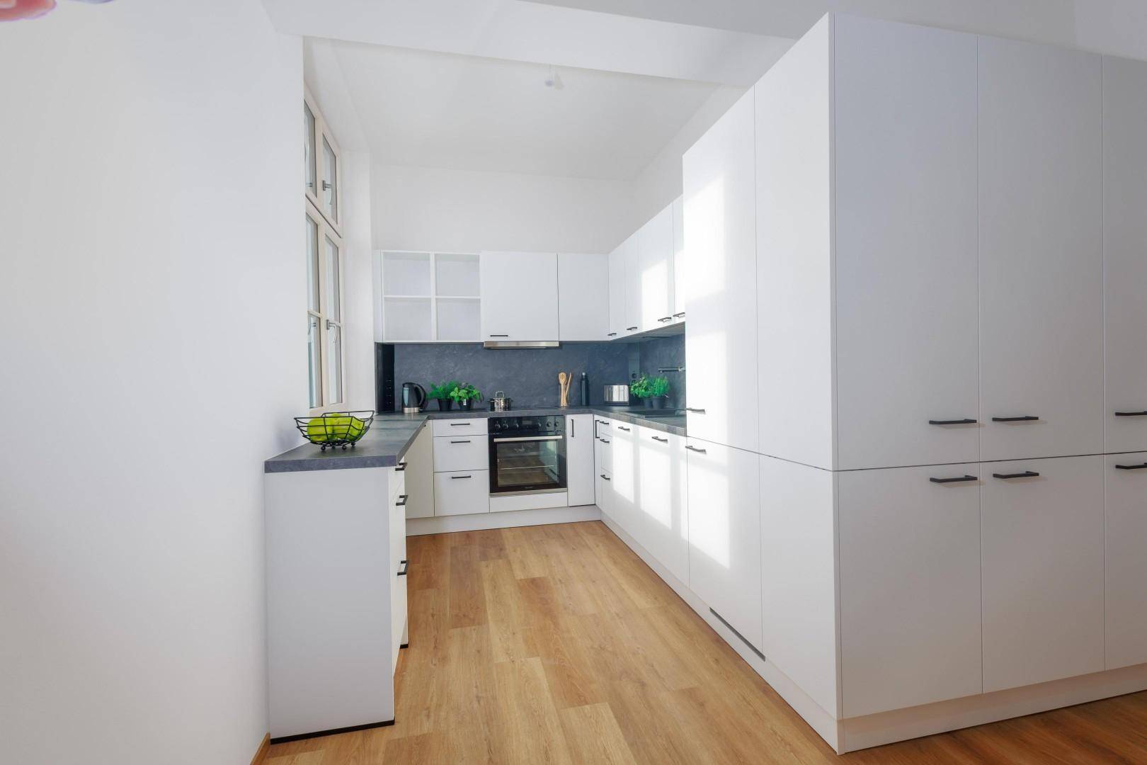 Lichtdurchflutete Küche mit weißen Schränken, dunkler Arbeitsplatte, Holzfußboden und Fenster.