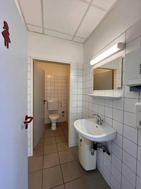 Gefliestes WC mit Waschbecken, Spiegel und separater Toilettenkabine.