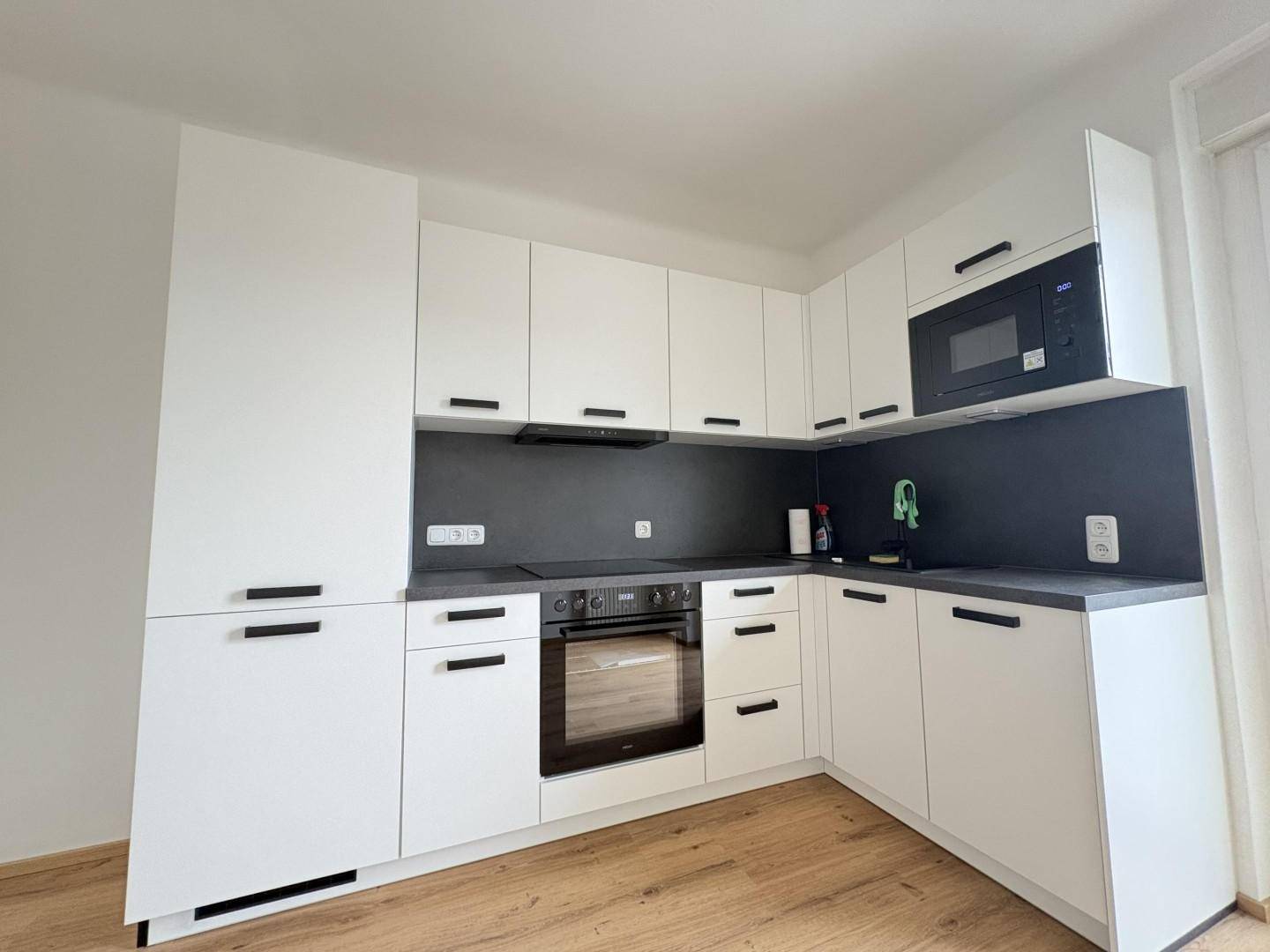 Moderne, neuwertige Küche mit weißen Schränken, integrierten Geräten und dunkler Arbeitsplatte.