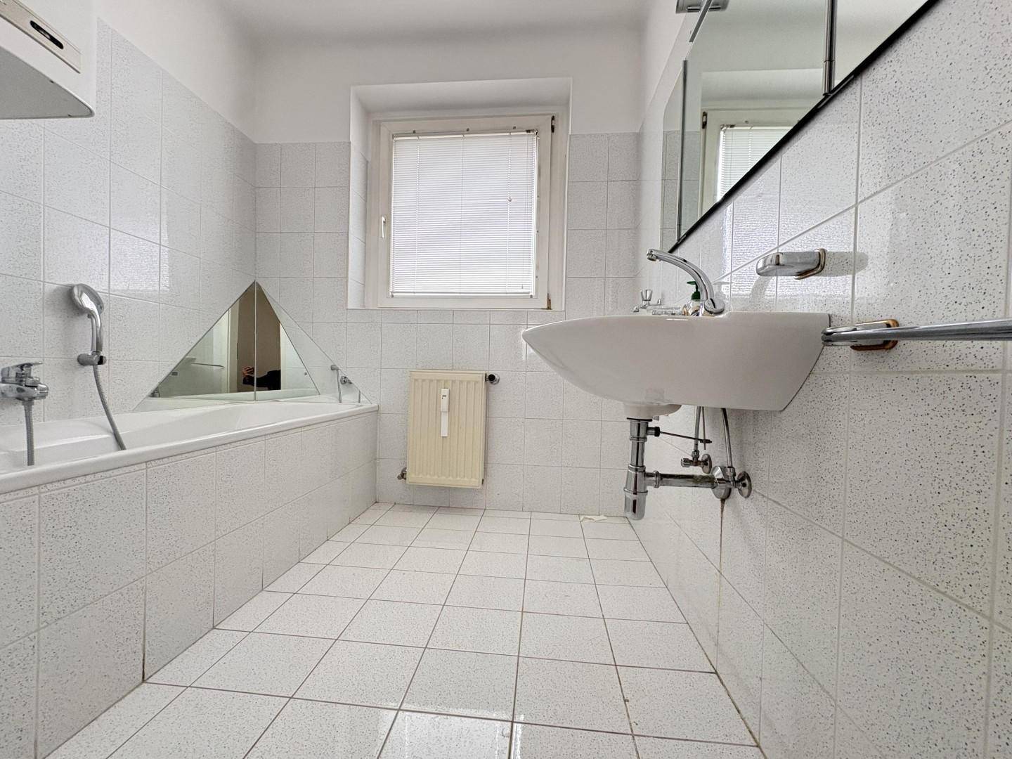 Gefliestes Badezimmer mit Badewanne, Waschbecken und einem Fenster für natürliche Belüftung.