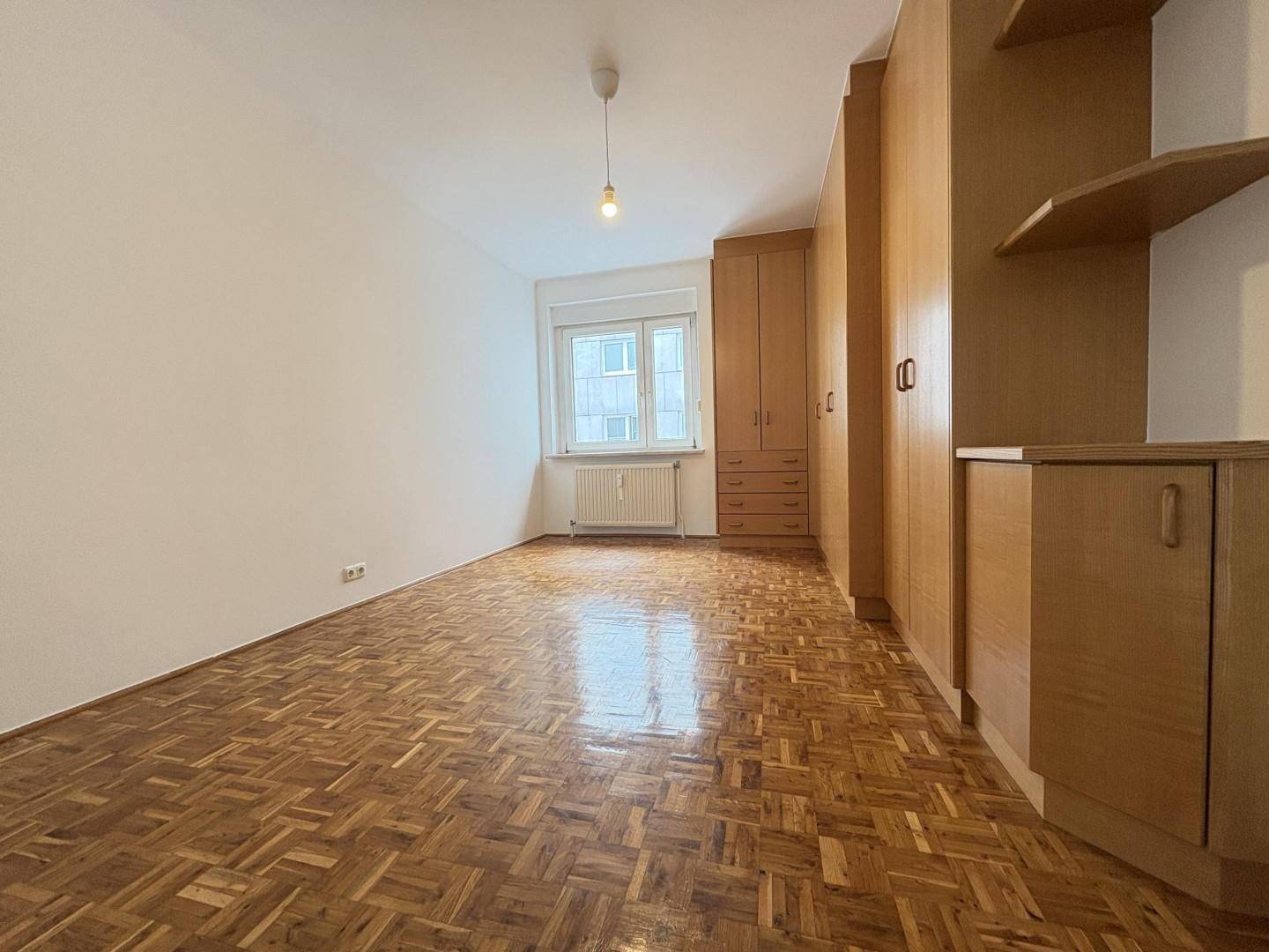Geräumiges Schlafzimmer mit Parkettboden, Einbauschränken und einem großen Fenster.