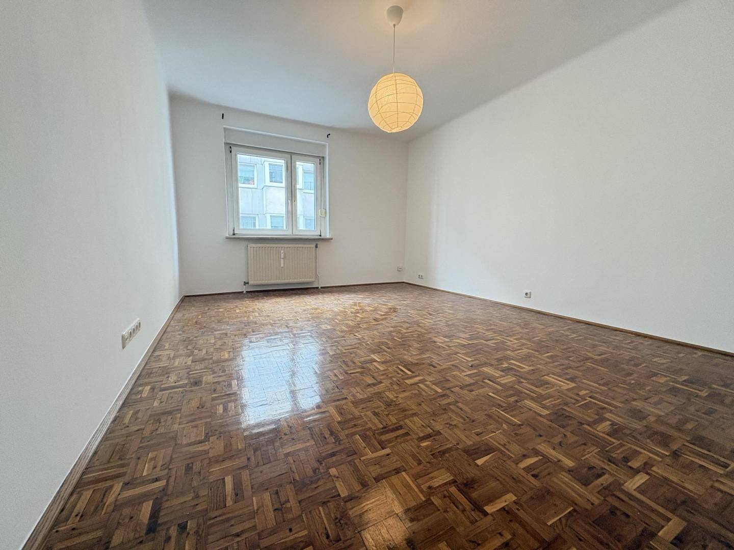 Helles Schlafzimmer mit glänzendem Parkettboden und einem großen Fenster für viel Tageslicht.