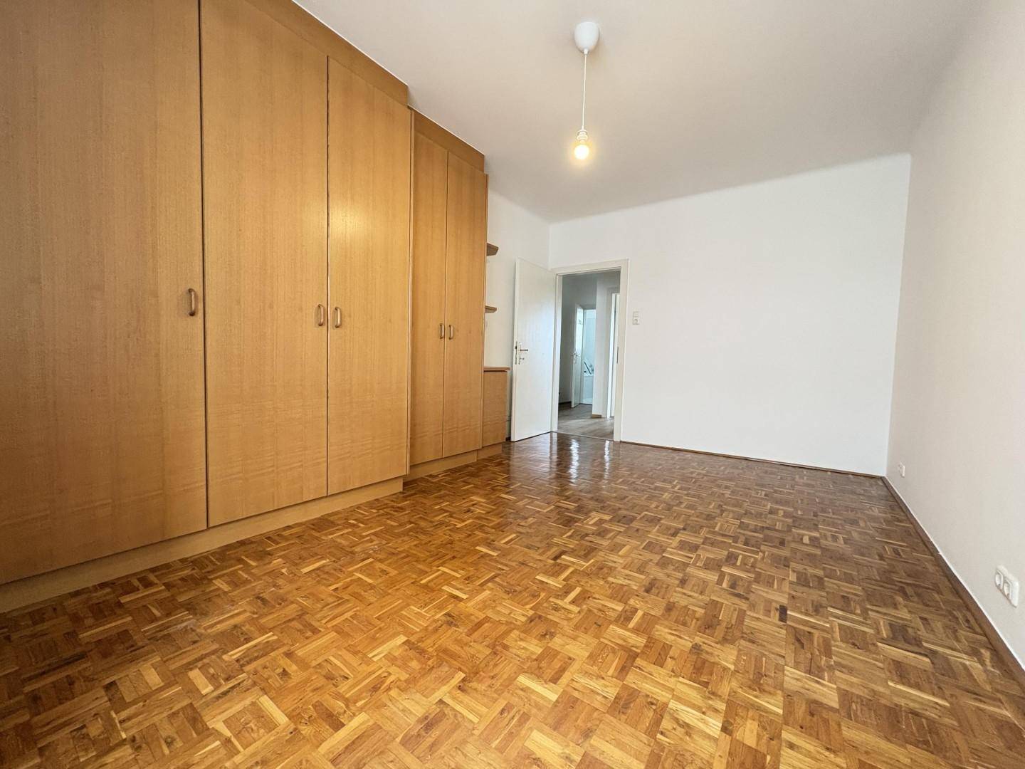 Schlafzimmer mit klassischem Parkettboden und raumhohen, holzfarbenen Einbauschränken.