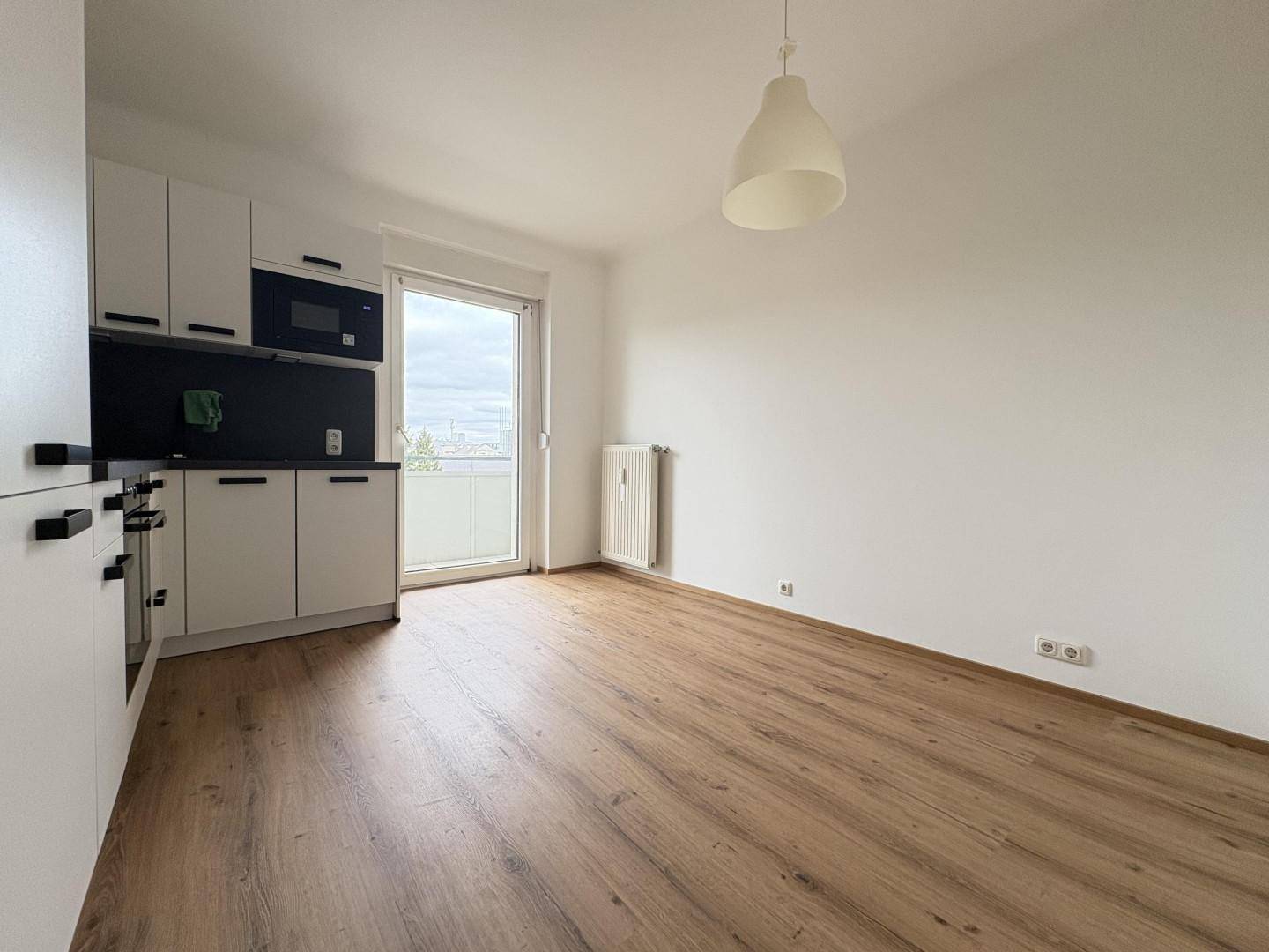 Heller Wohnbereich mit Laminatboden, weiß gestrichenen Wänden und Zugang zu einem Balkon.