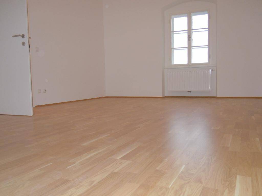 Helles Schlafzimmer mit Parkettboden und einem Fenster, das viel Tageslicht hereinlässt.