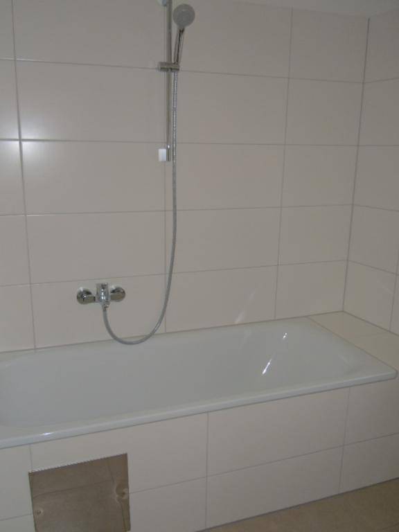 Badezimmer mit einer Badewanne und integrierter Duschfunktion, umgeben von hellen Fliesen.