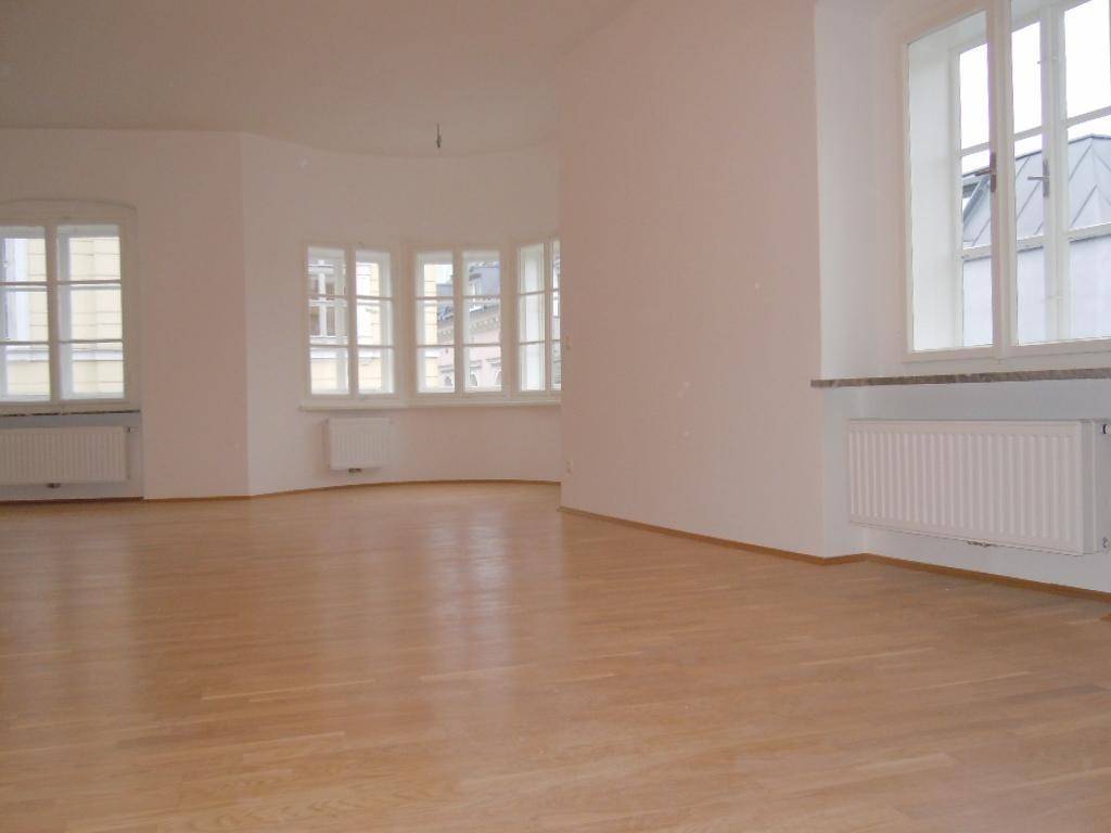 Geräumiges Wohnzimmer mit hellem Parkettboden und vielen Fenstern für viel Tageslicht.