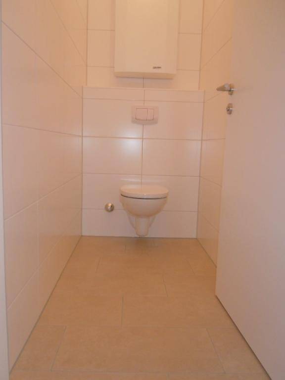 Separates WC mit wandhängender Toilette und hellen Fliesen an Wänden und Boden.