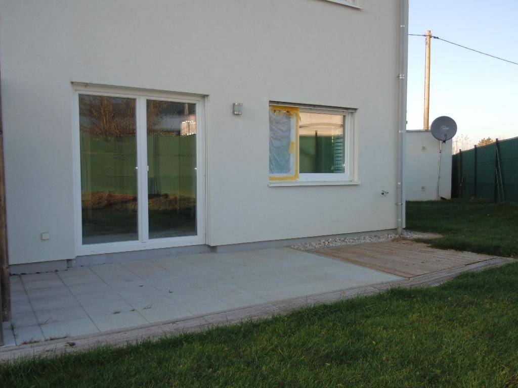 Hinteransicht des Hauses mit einer kleinen gepflasterten Terrasse und direktem Zugang zum Garten.