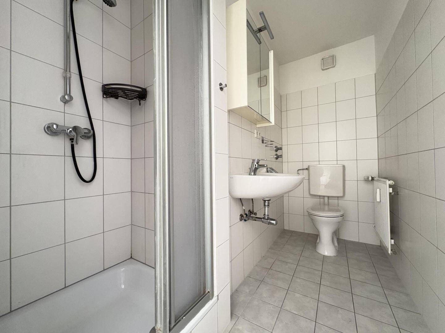 Funktionales Badezimmer mit weißen Fliesen, Duschkabine, Waschbecken und Toilette.
