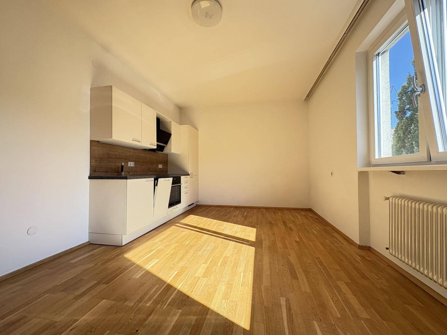 Geräumiger, heller Raum mit Holzboden und moderner Küchenzeile, mit Blick ins Grüne.