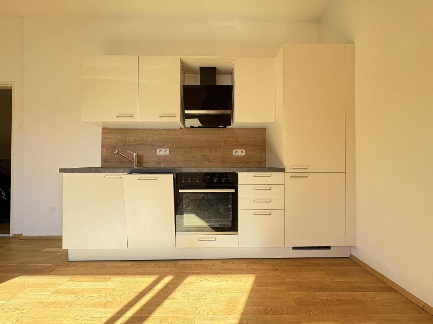 Moderne, weiße Einbauküche mit integriertem Backofen und Dunstabzugshaube in hellem Raum.