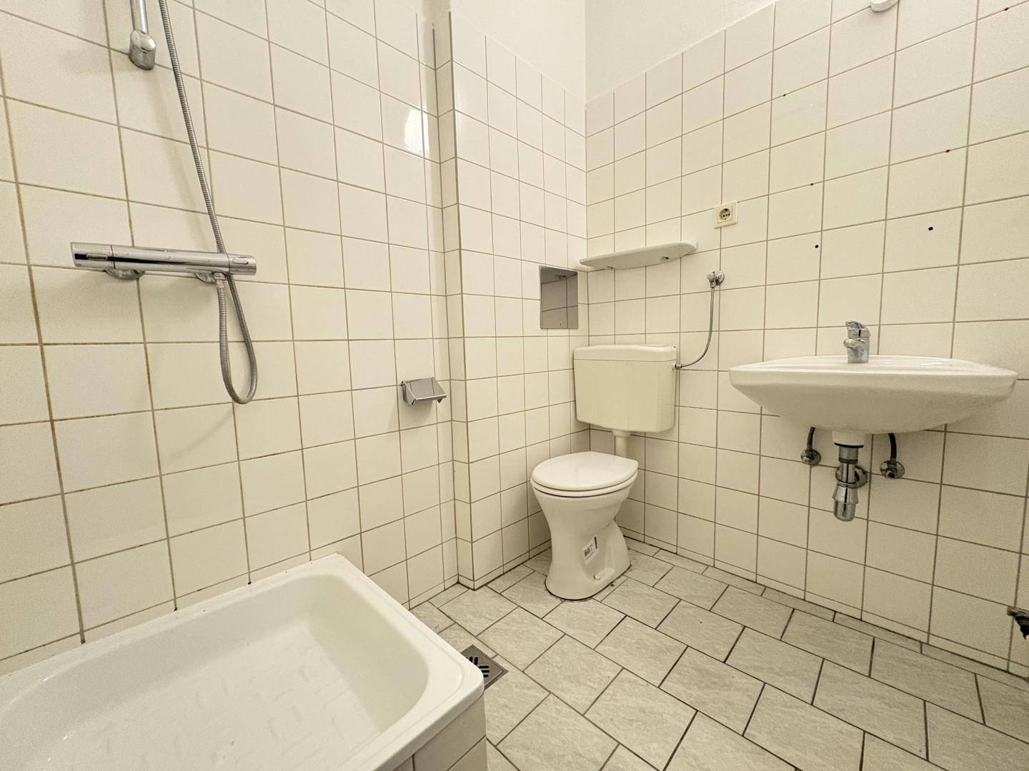 Gefliestes Badezimmer mit Badewanne, Toilette und Waschbecken in schlichtem Design.