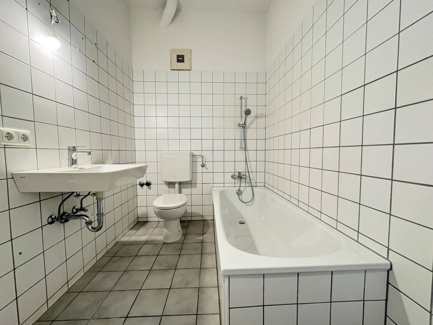 Gefliestes Badezimmer mit Badewanne, Toilette und Waschbecken in schlichtem Design.