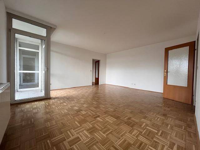 Geräumiges Wohnzimmer mit Parkettboden und Zugang zu einem hellen Balkon, ideal für Entspannung.