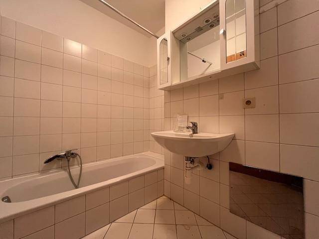 Badezimmer mit Badewanne, Waschbecken und weißen Fliesen, in einem sauberen und funktionalen Zustand.