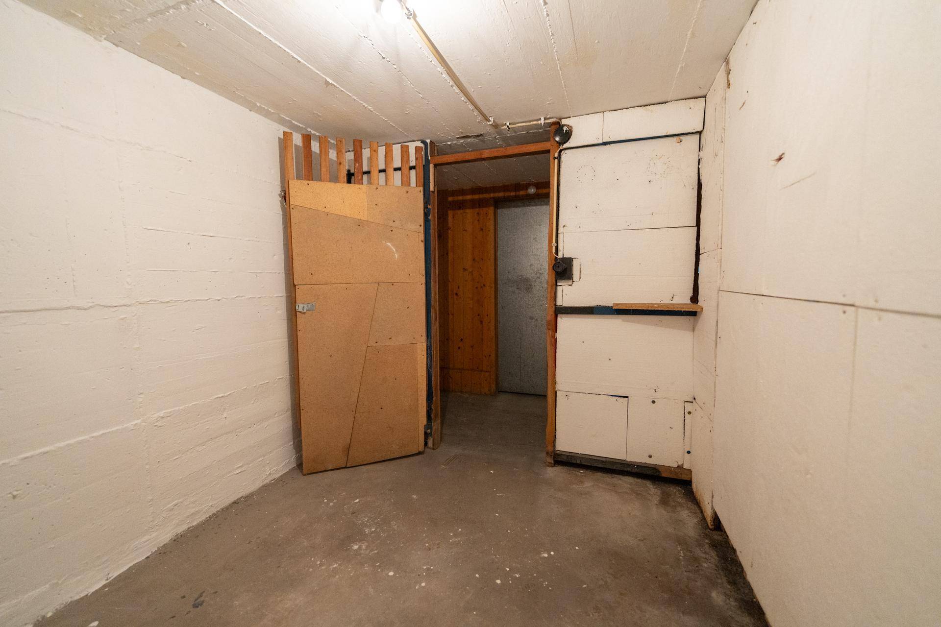 Eingang zu einem Abstellraum im Keller mit einfachen Holztüren und Betonboden.