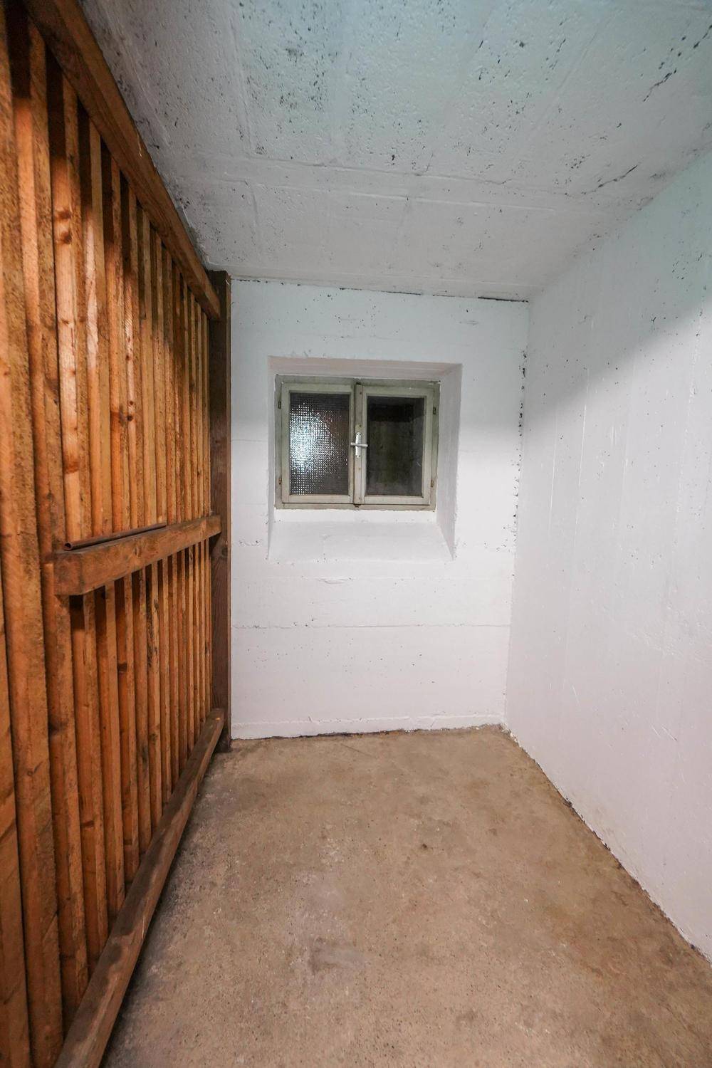 Kellerraum mit Betonboden, weiß gestrichenen Wänden und einem kleinen Fenster zur Belüftung.
