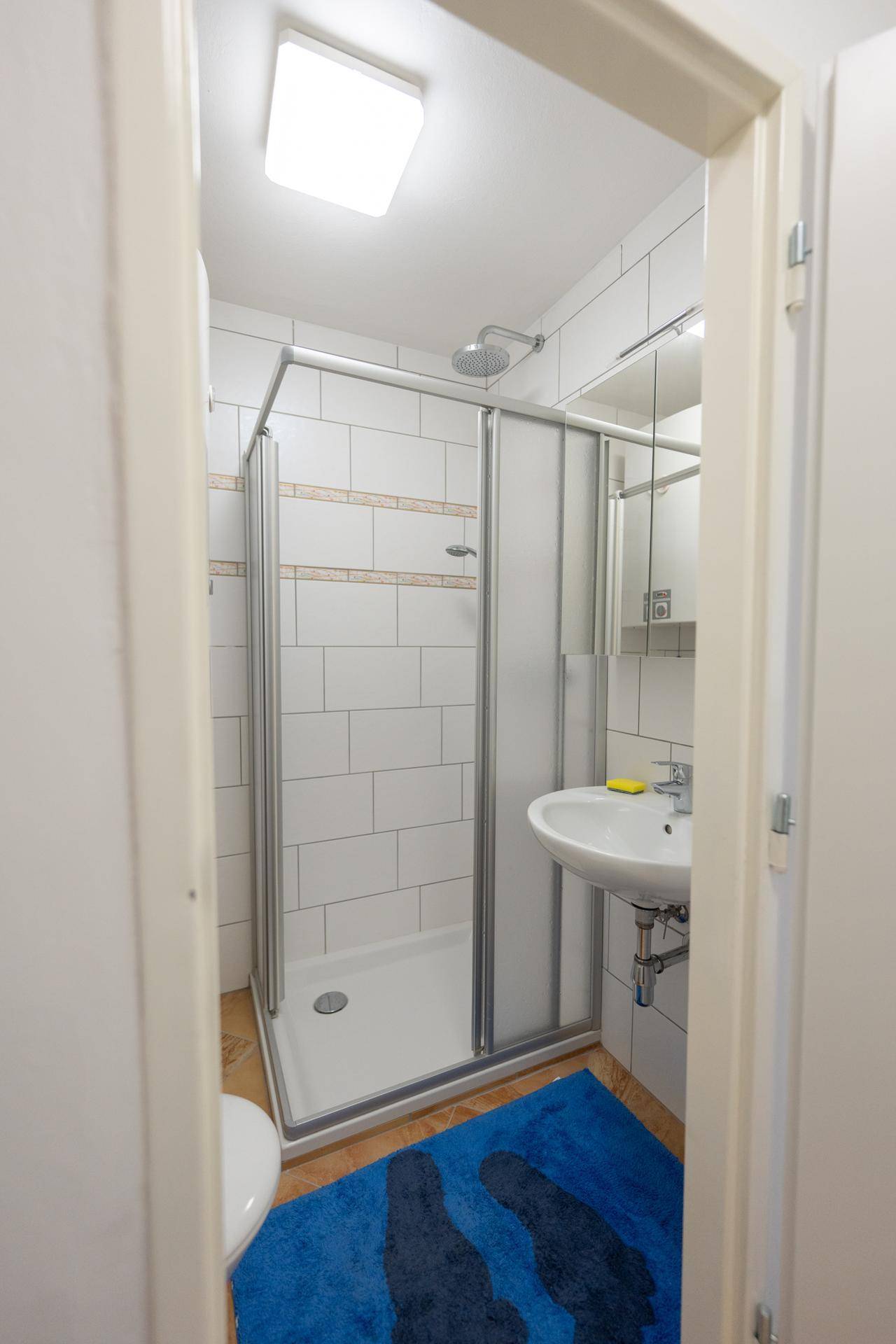 Badezimmer vom Türrahmen aus gesehen, mit Dusche, Waschbecken und Toilette.
