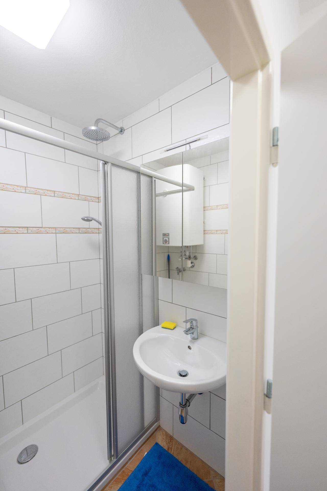 Kleines Badezimmer mit Dusche, Waschbecken und weißen Fliesen.