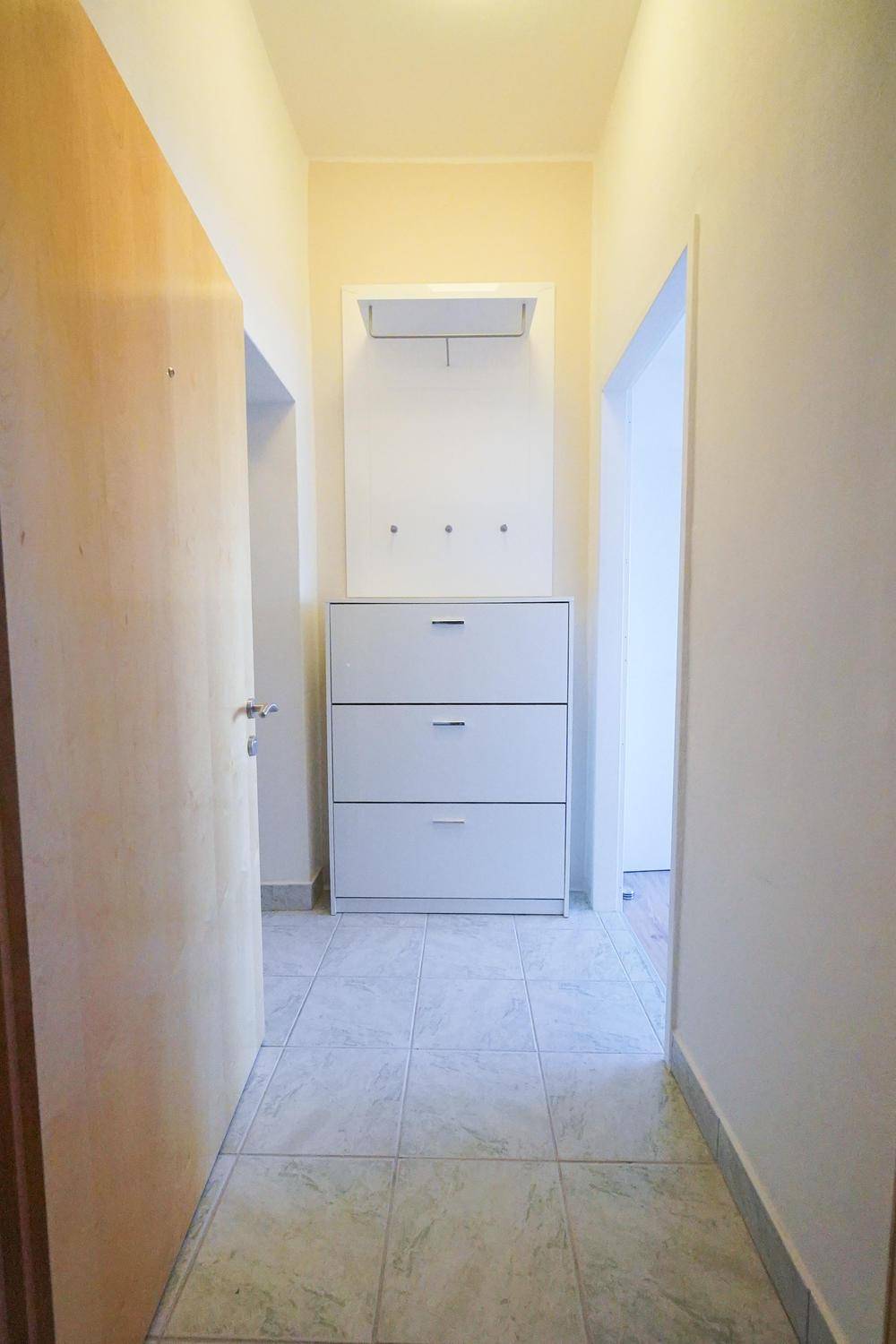 Heller Flur mit Fliesenboden und einer praktischen Garderobenlösung für Schuhe und Mäntel.