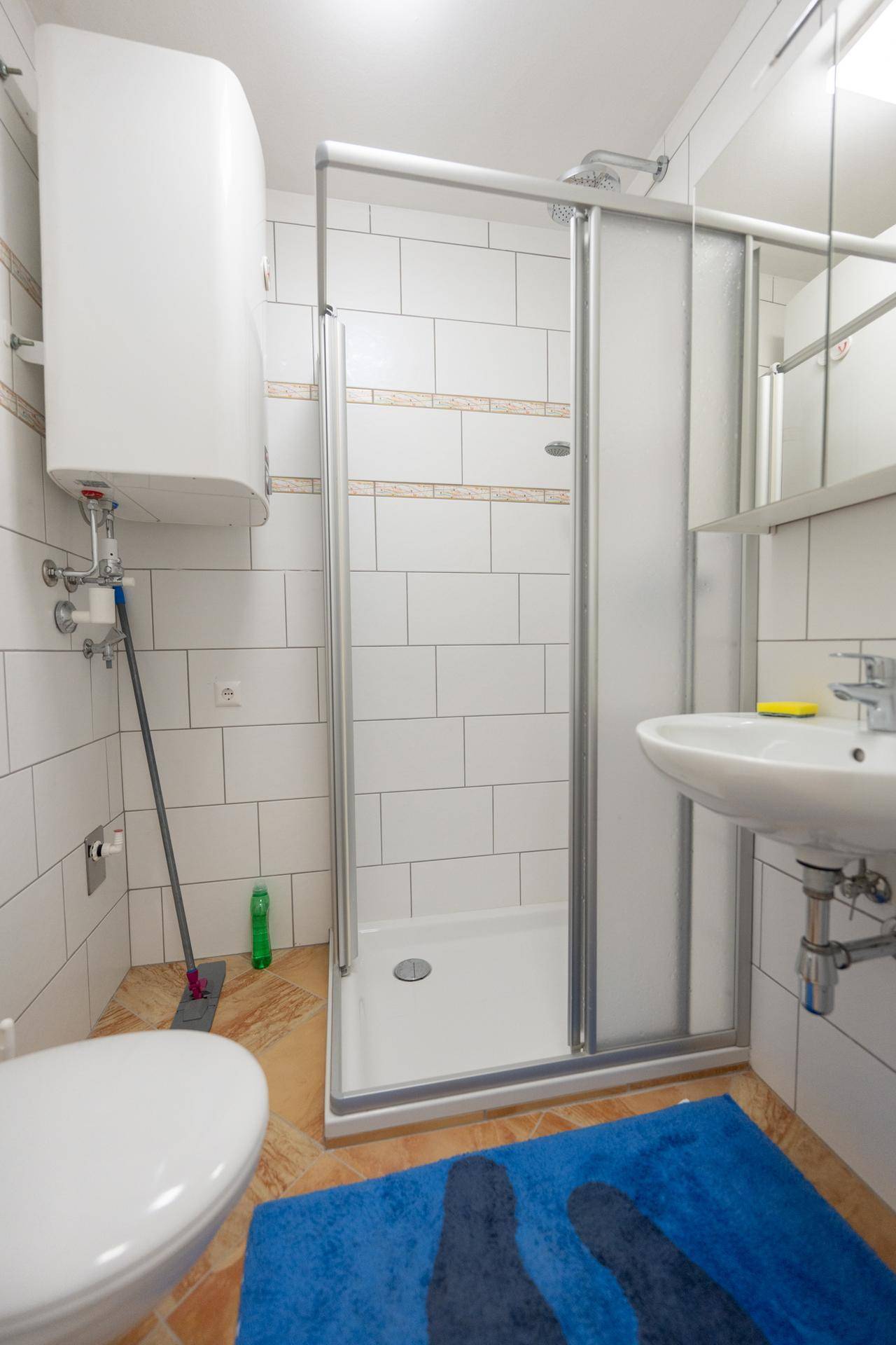 Badezimmer mit Toilette, Duschkabine und einem an der Wand montierten Warmwasserboiler.