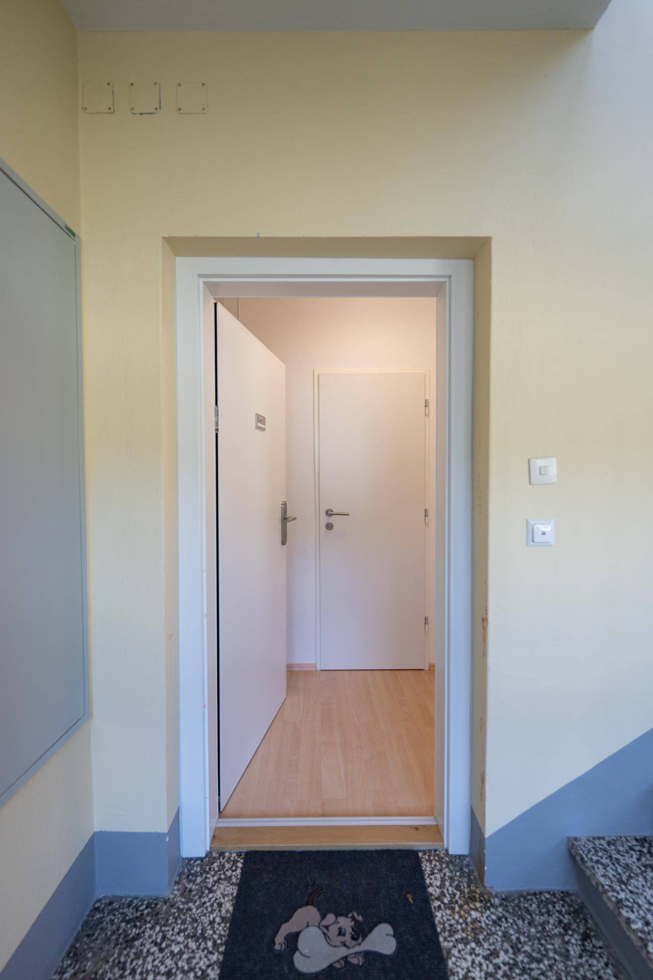 Offene Wohnungstür gibt den Blick frei auf einen hellen Flur mit Holzfußboden.