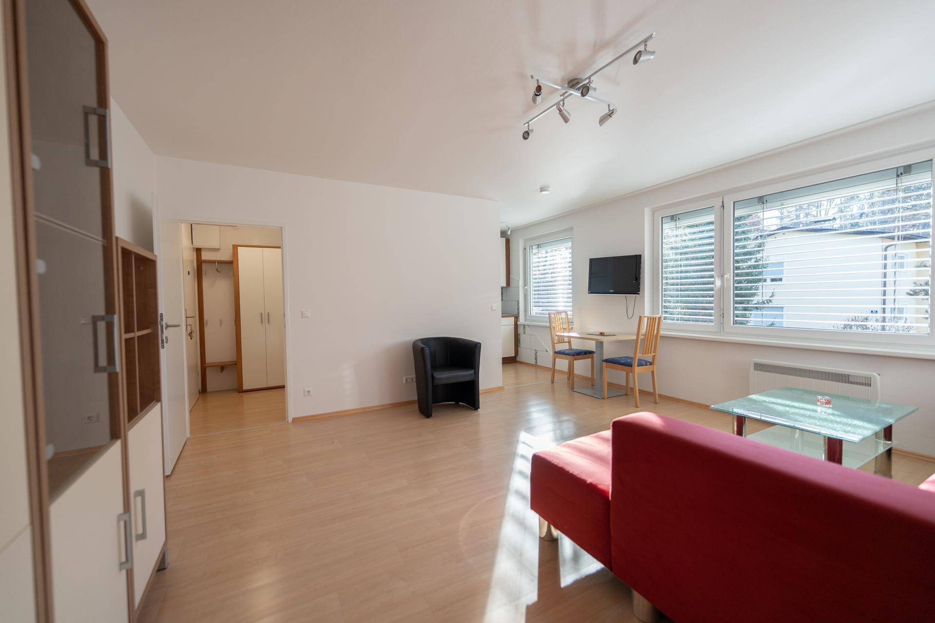 Wohnzimmer mit hellem Holzfußboden, das zum Flur und zur Küche hin offen ist.