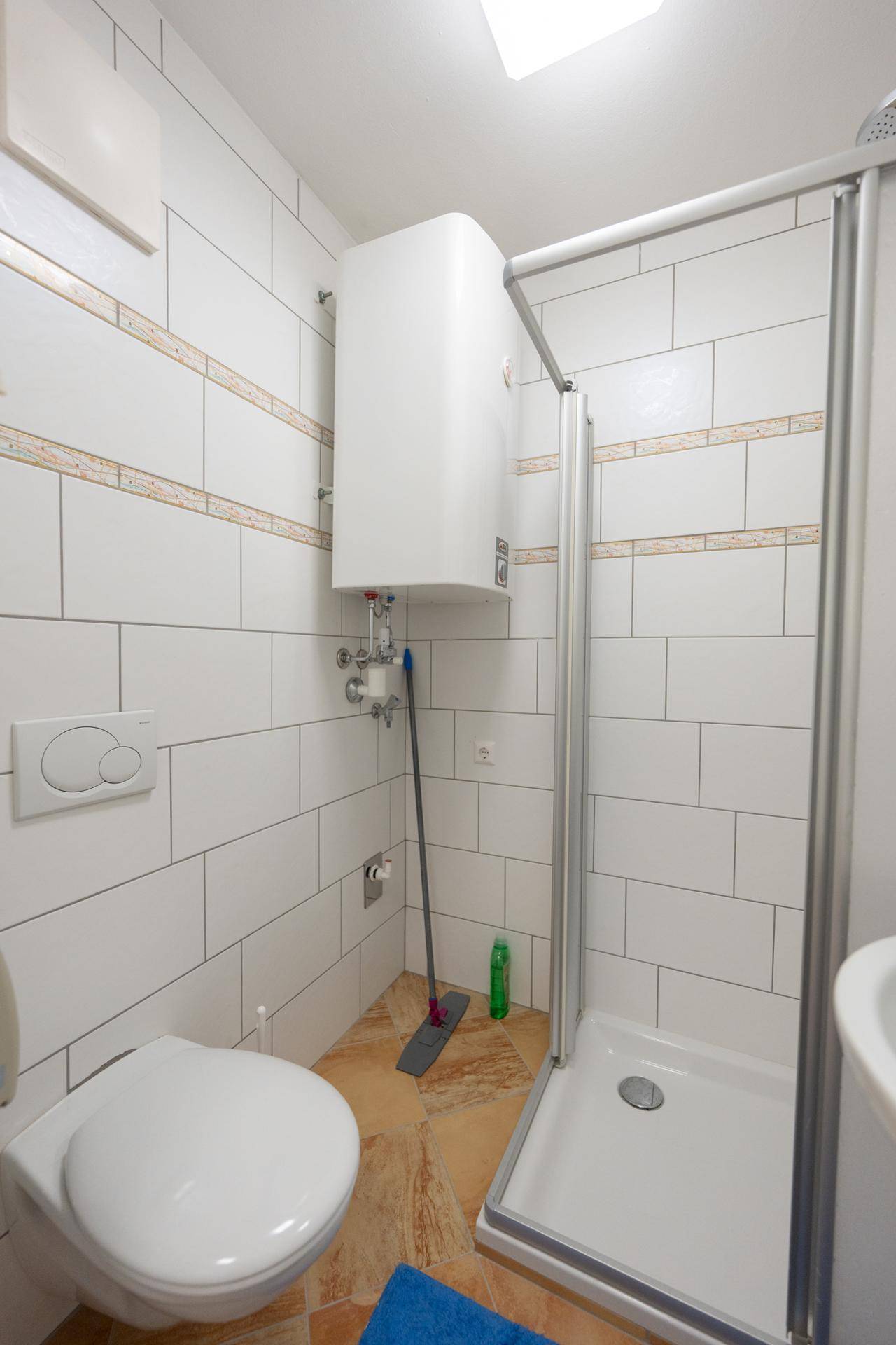 Badezimmer mit Toilette, Duschkabine und Boiler an der Wand.