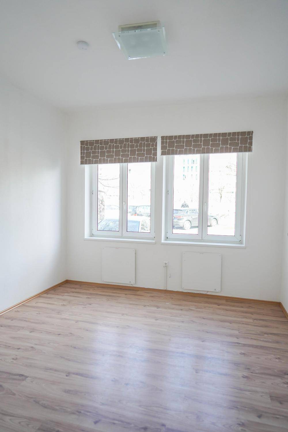 Heller, leerer Raum mit zwei großen Fenstern und einem pflegeleichten Laminatboden, ideal als Wohnbereich.
