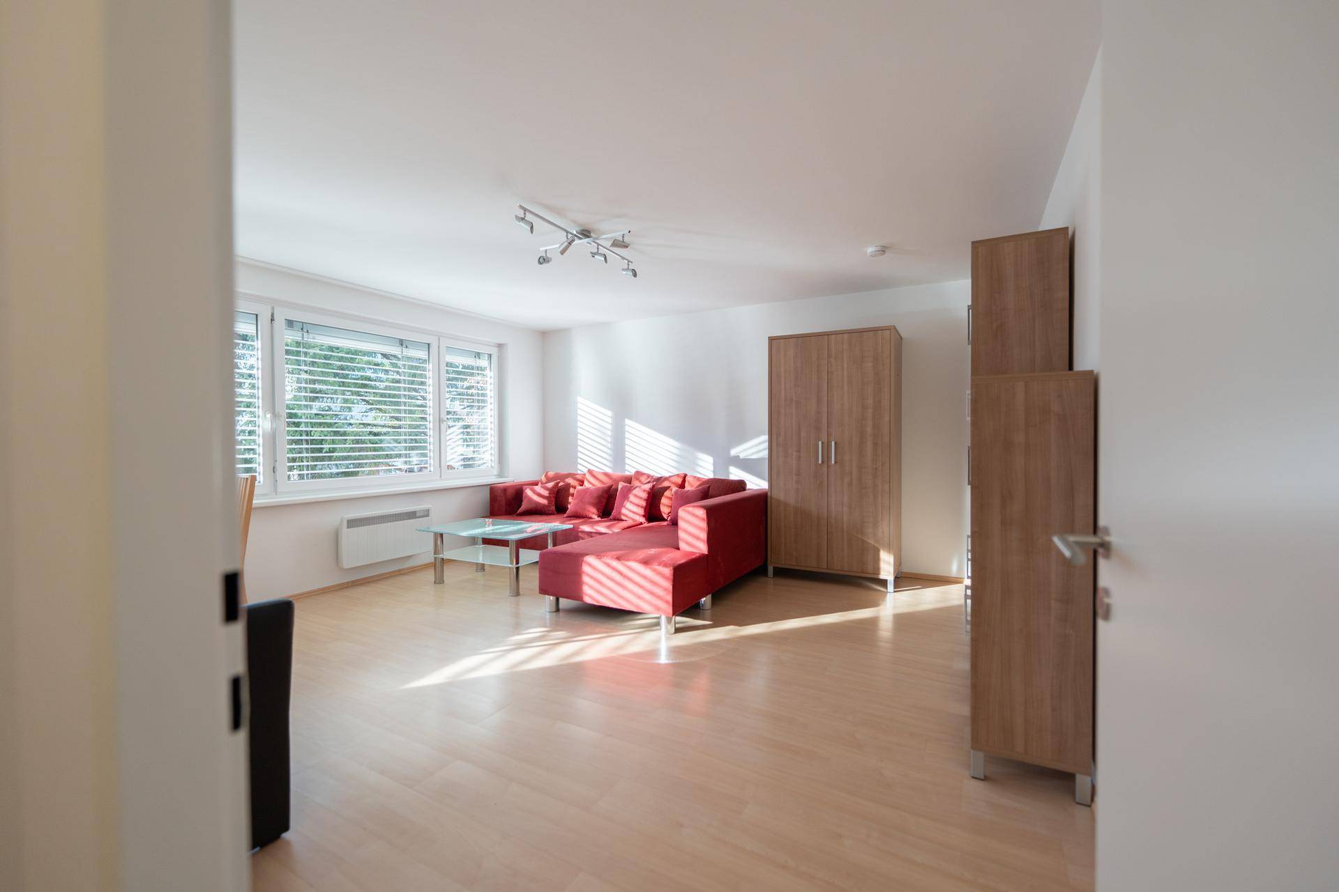 Geräumiges Wohnzimmer mit hellem Holzfußboden, rotem Sofa und großen Fenstern.