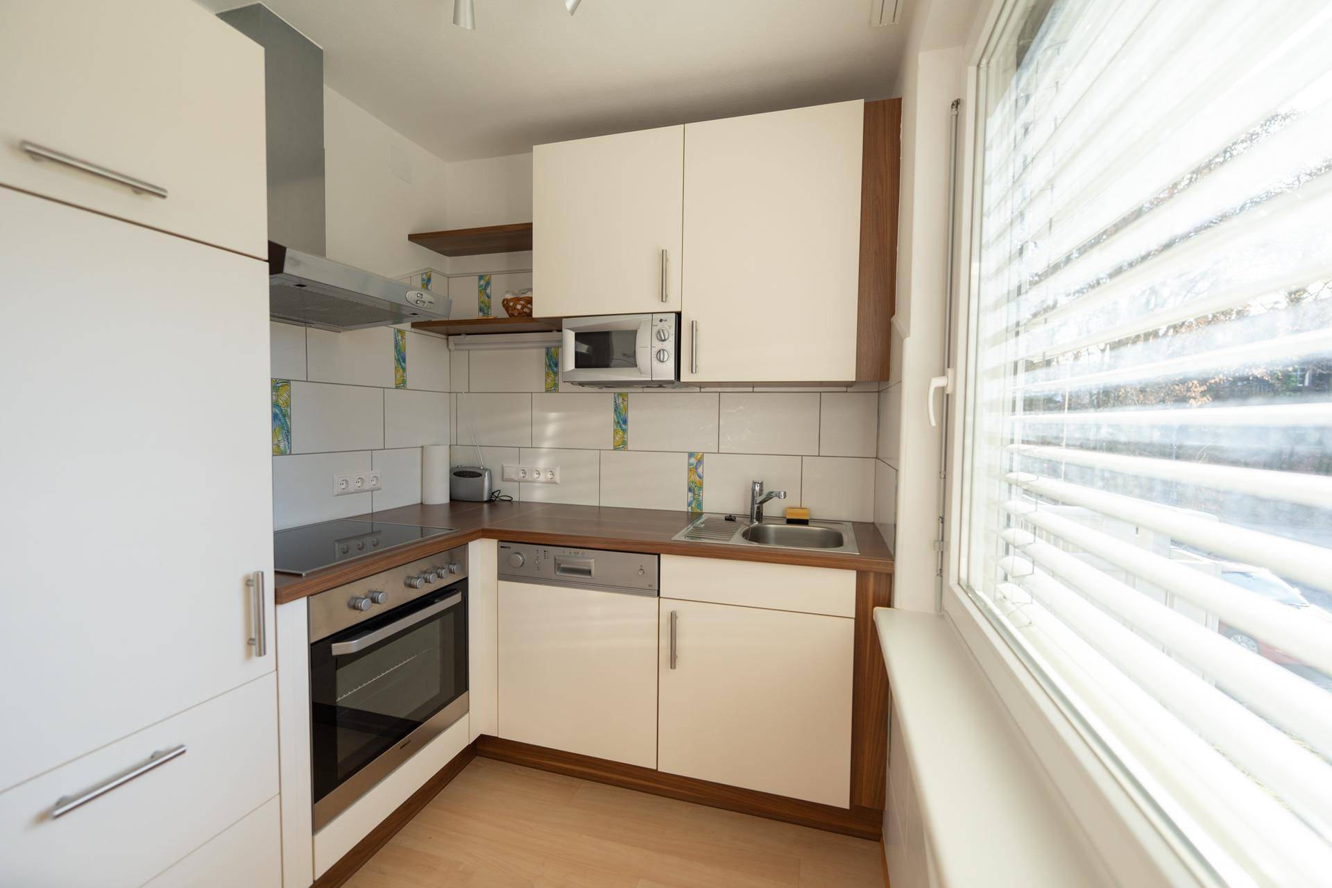 Helle Küche mit weißen Schränken, Einbaugeräten und einem Fenster mit viel Tageslicht.