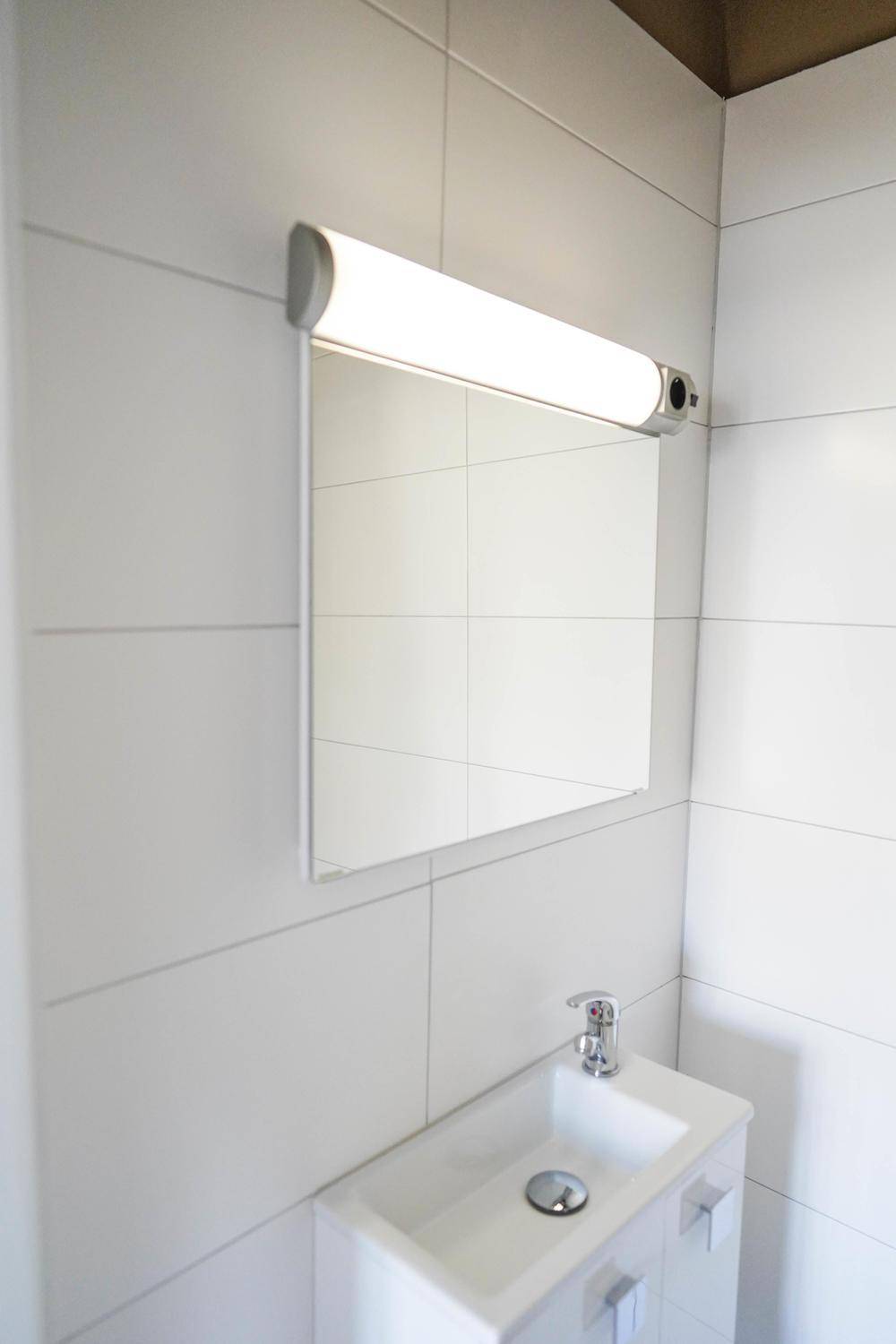 Modernes Badezimmer mit kleinem Waschbecken, Spiegel und weiß gefliesten Wänden, sauber und funktional.