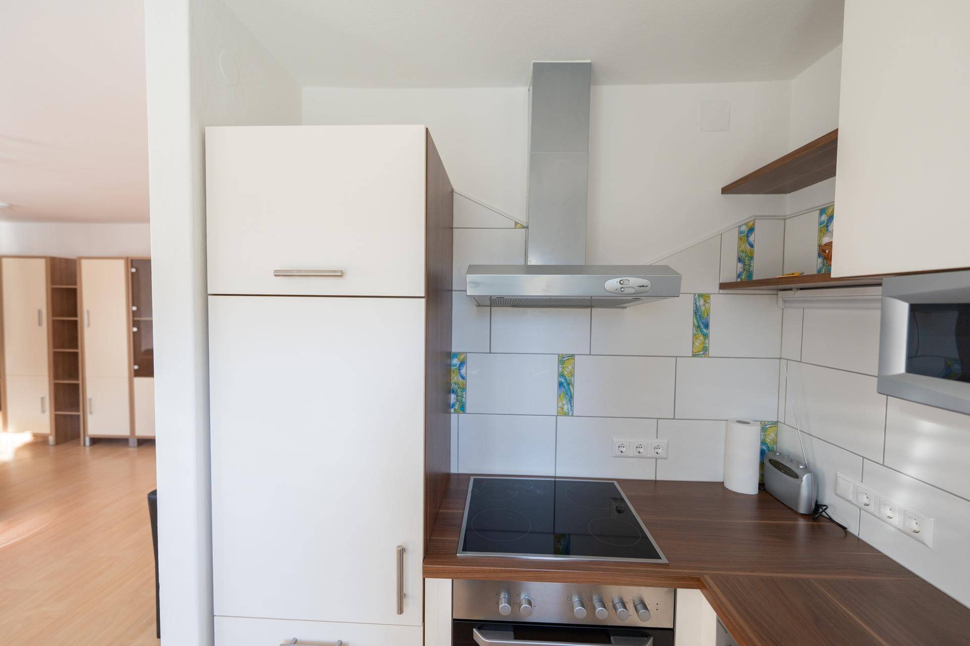 Detailansicht der Küche mit weißen Schränken, Dunstabzugshaube und Fliesenrückwand.