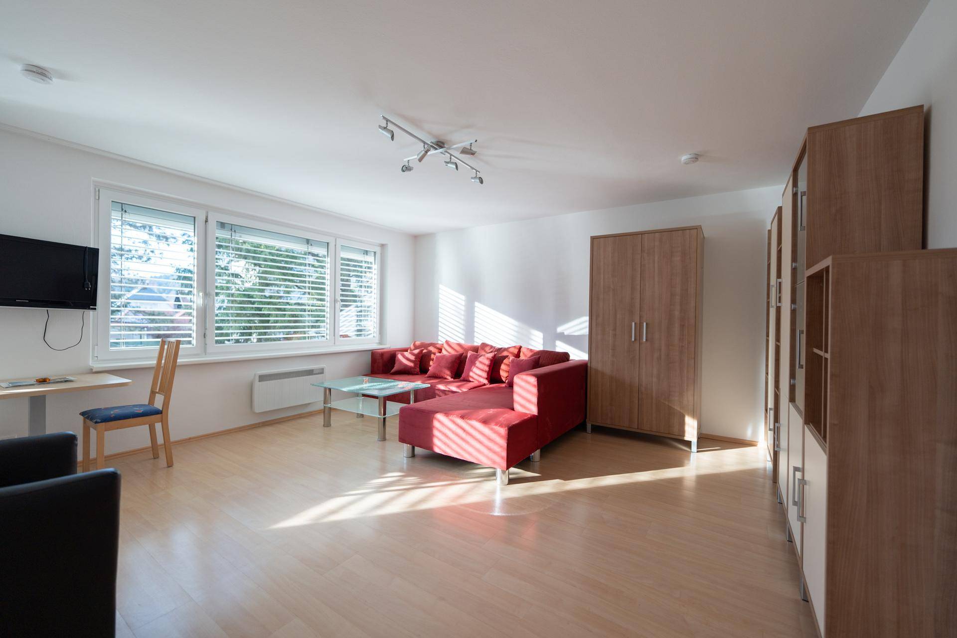 Helles Wohnzimmer mit rotem Sofa, Holzmöbeln und viel Tageslicht durch große Fenster.