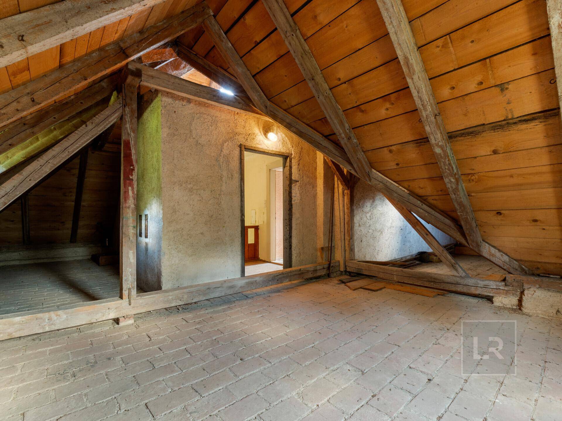 Unausgebauter Dachboden mit sichtbaren Holzbalken und Ziegelboden, bietet Ausbaupotenzial.