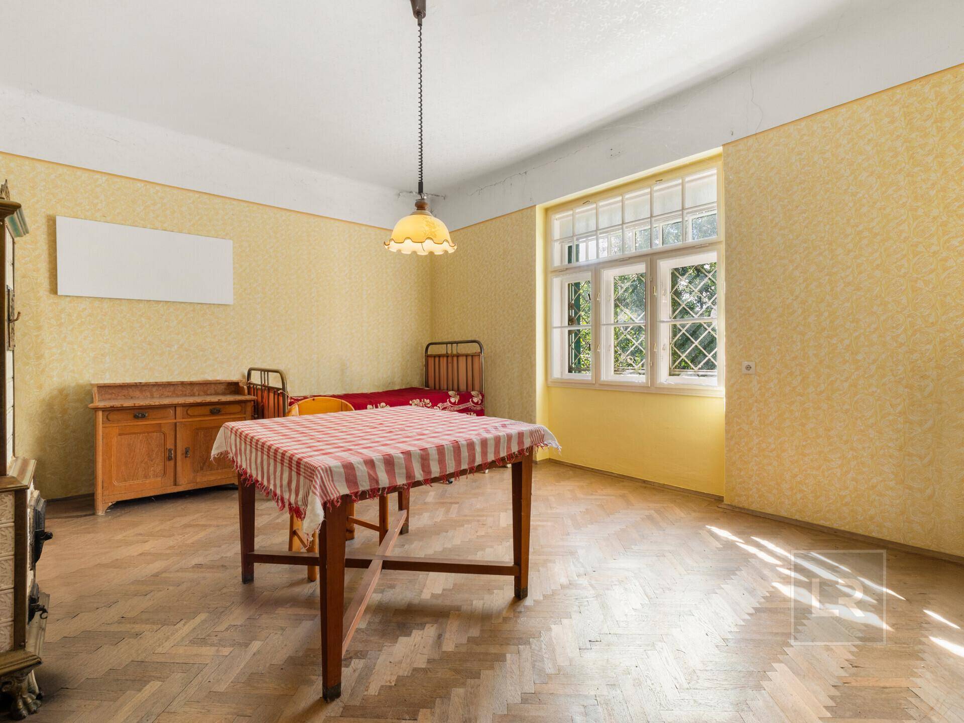 Helles Zimmer mit Fischgrätparkett, gelber Tapete und einem Fenster mit Blick ins Grüne.