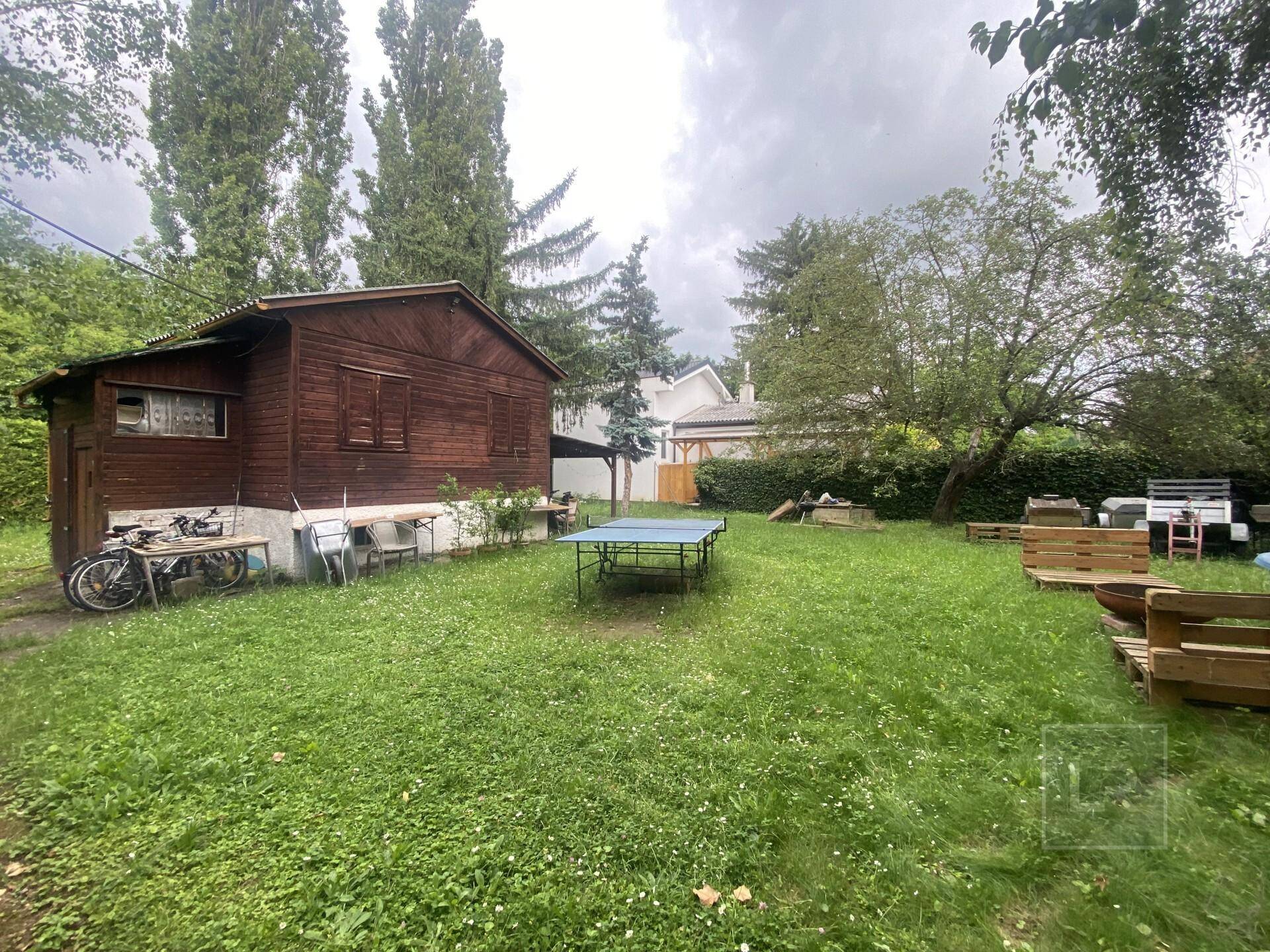 Garten mit Holzschuppen, Rasenfläche und einer Tischtennisplatte für Freizeitaktivitäten.